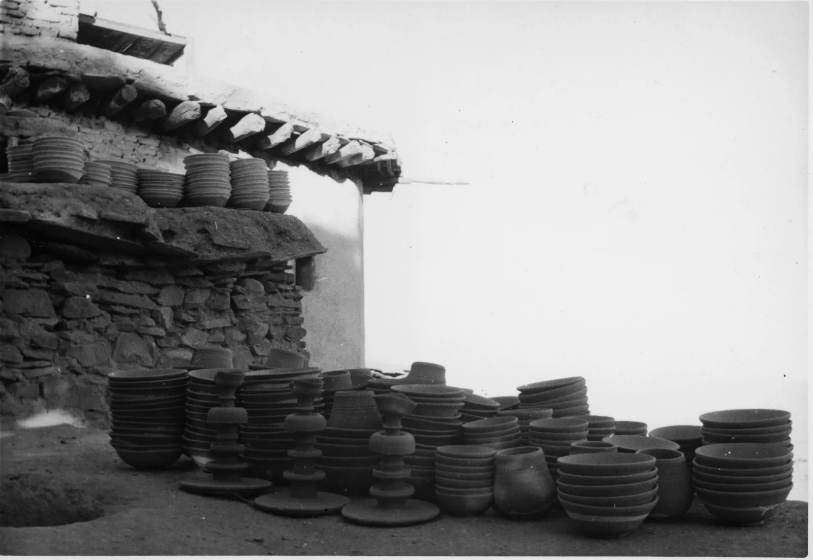 Historical photograph of pottery stacked outside a house in Istalif